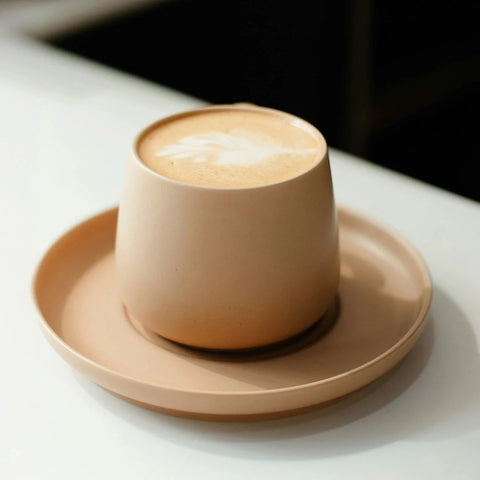 Cappuccino in a beige cup on a matching saucer on a white surface